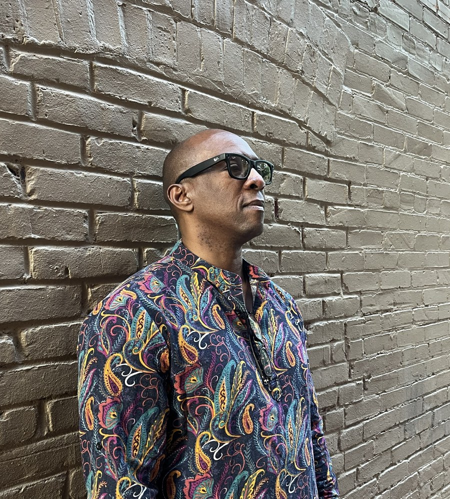 Boris Willis outdoors against a brick wall, wearing a patterned shirt and sunglasses