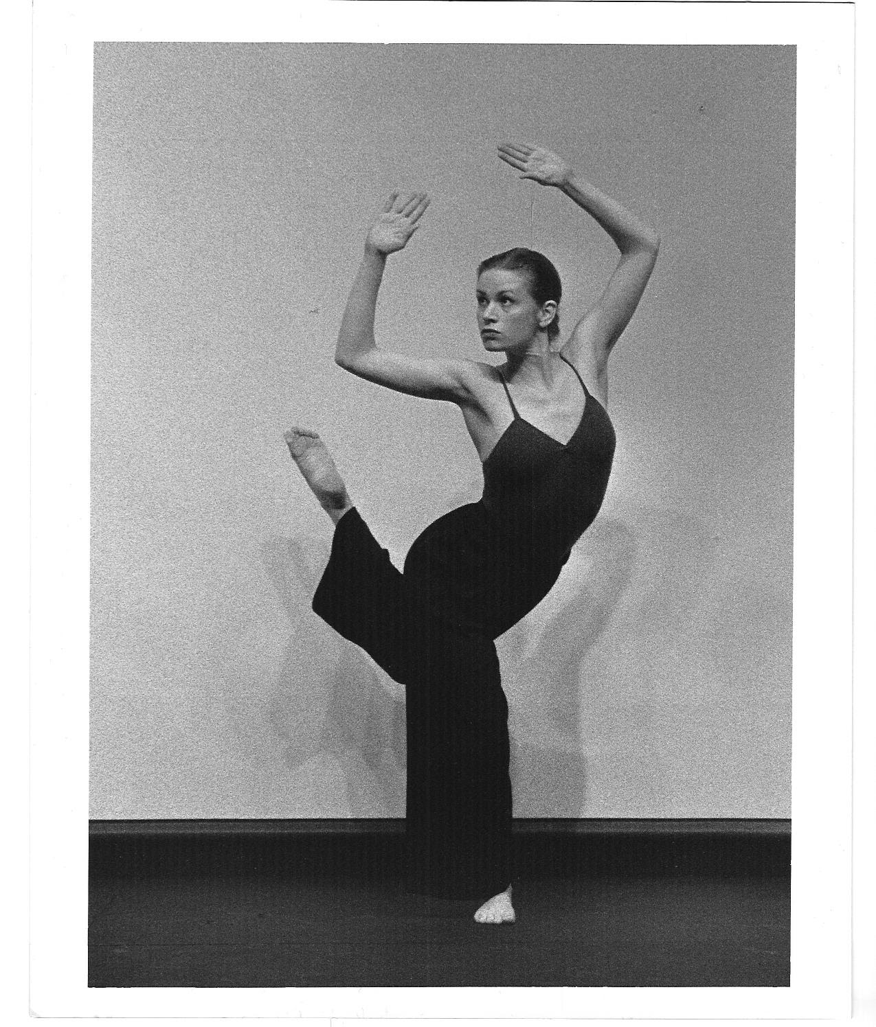 Cynthia McLaughlin in a studio, balanced on one leg with the other lifted to the side, arms framed overhead