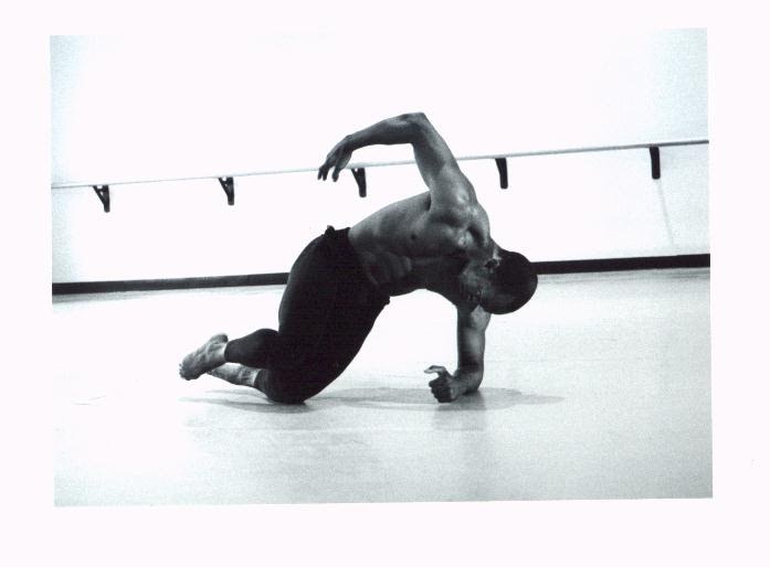 Black-and-white photograph of Boris Willis low to the floor in a crouching dance pose, one arm arcing overhead