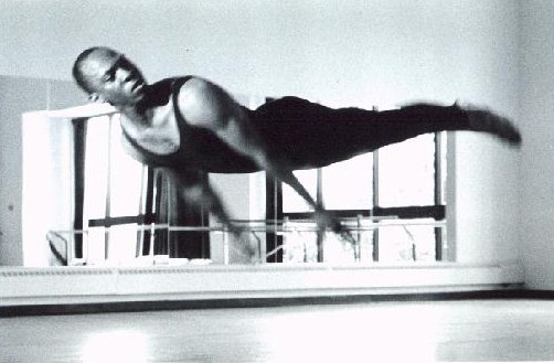 Black-and-white photograph of Boris Willis in a horizontal side balance against the ballet barre, legs extended