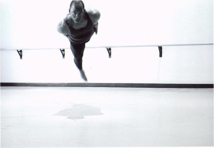 Black-and-white photograph of Boris Willis leaping toward the camera, seen from above over the ballet barre