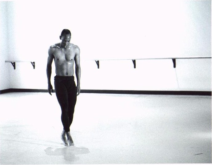 Black-and-white photograph of Boris Willis walking forward across the studio, head lowered