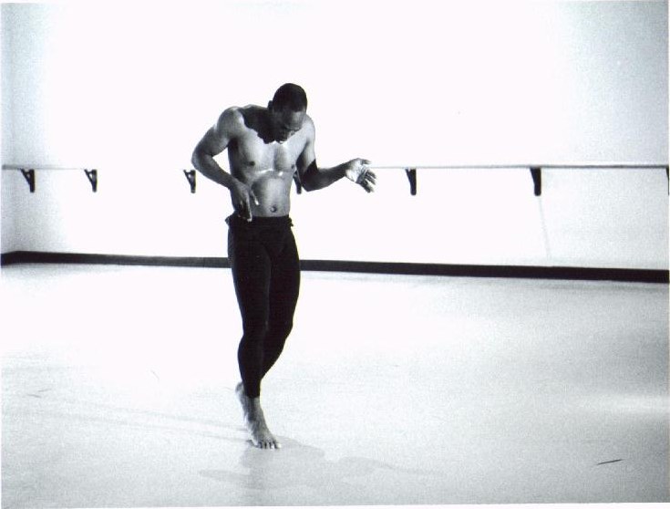Black-and-white photograph of Boris Willis standing, looking down, one hand raised