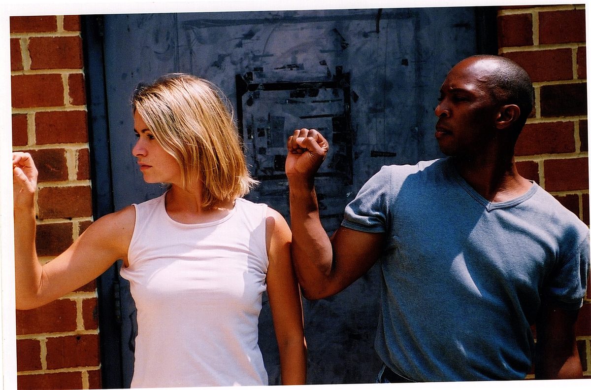 Boris Willis and Cynthia McLaughlin against a weathered wall, arms raised, in Enter Race