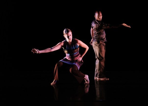 Cynthia McLaughlin crouching low as Boris Willis stands behind, dimly lit