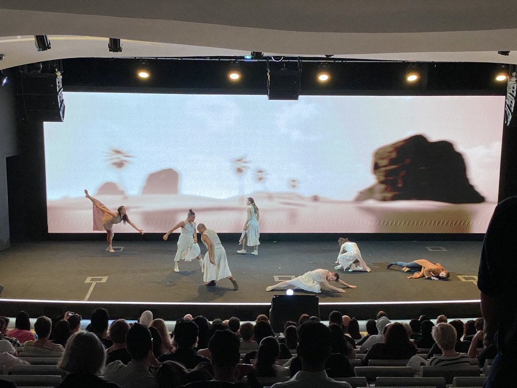 Company E performing before a rendered desert-and-sea environment