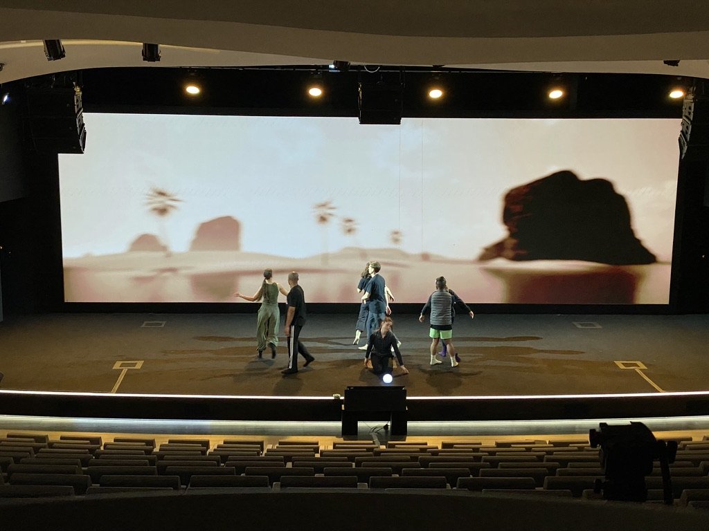 Dancers rehearsing in street clothes in front of the rendered desert scene