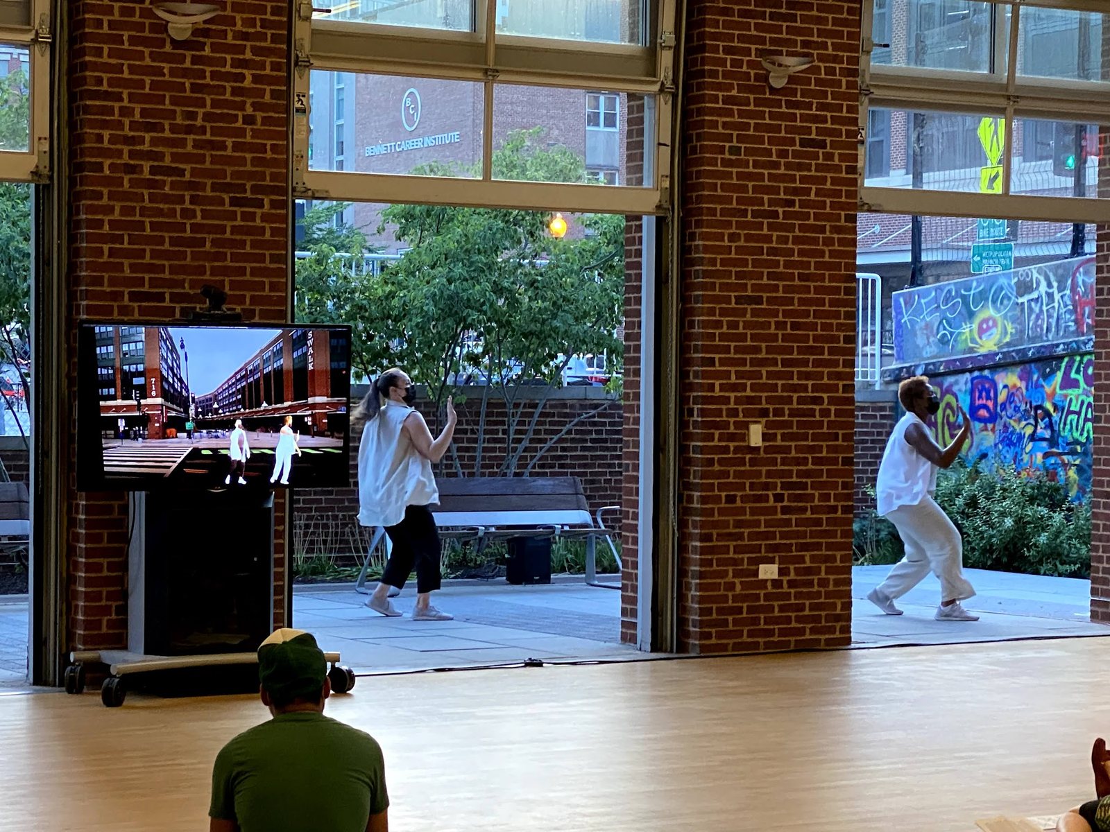 Two masked dancers in white performing live in front of a screen showing rendered avatars