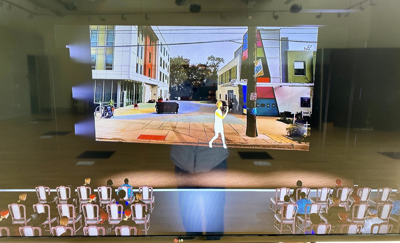 A large screen showing a rendered street with a motion-captured performer, watched by a rendered audience