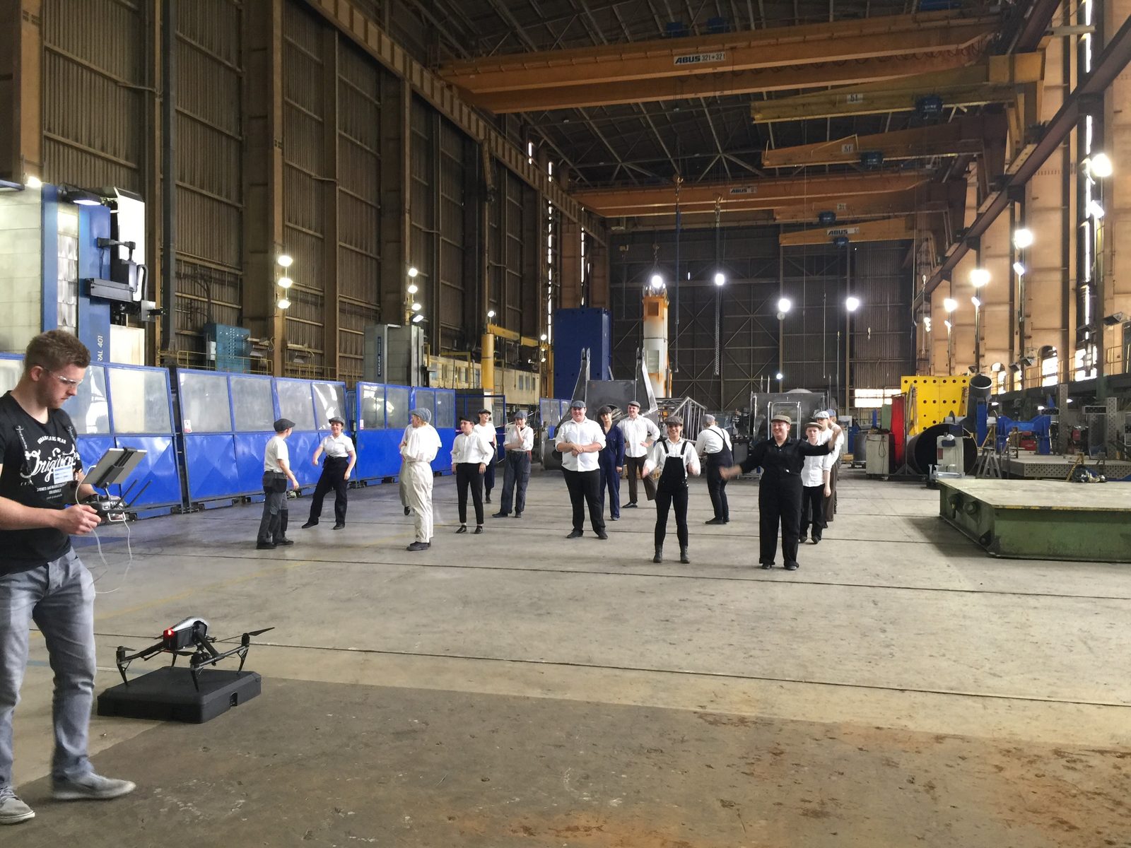 A drone operator films dancers spread across the factory floor