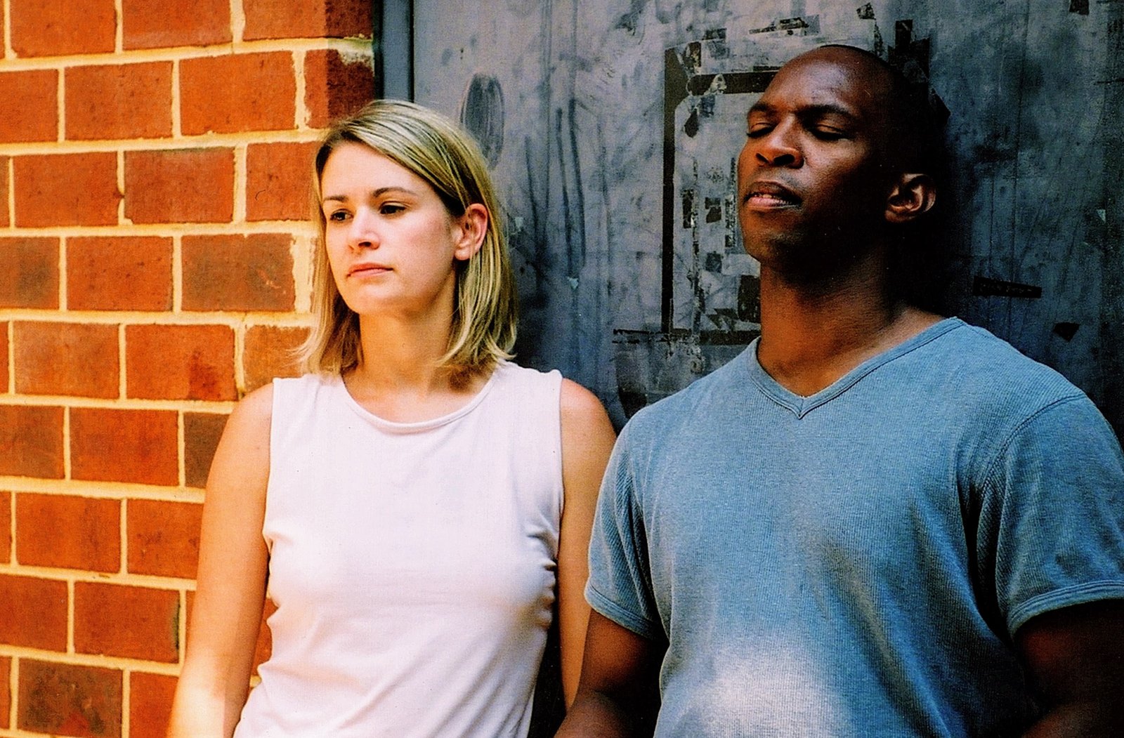 Boris Willis and Cynthia McLaughlin against a brick wall, eyes closed, in Enter Race