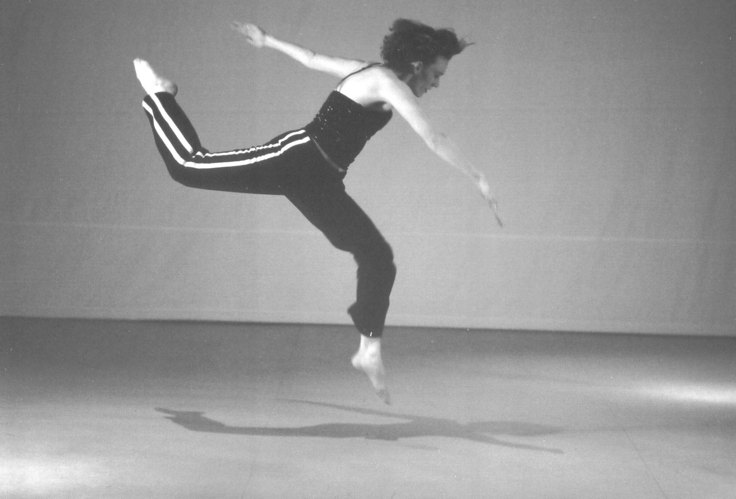 A dancer leaping with one leg extended behind, against a studio backdrop