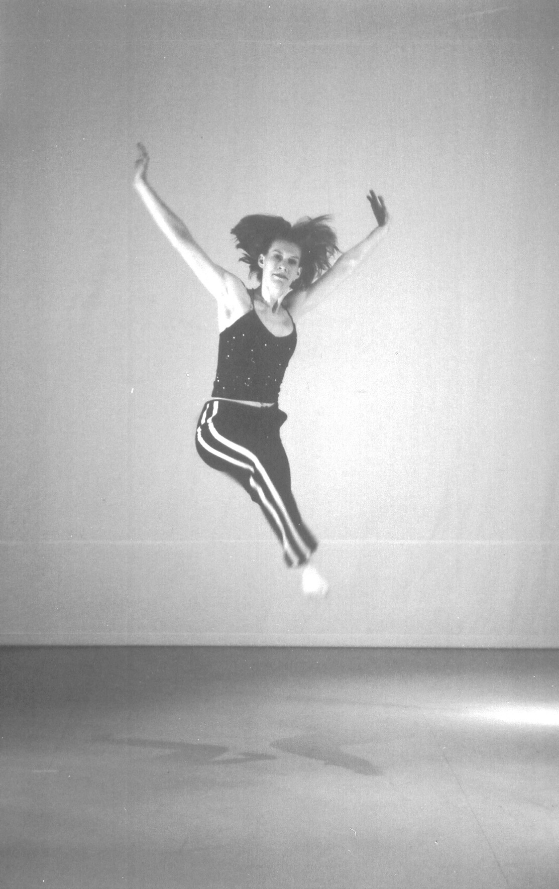 A dancer airborne with arms spread wide, against a studio backdrop
